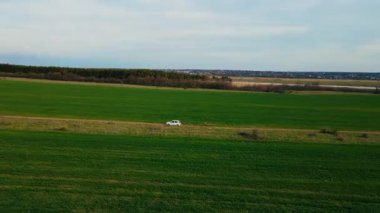 Country Road 'da hava manzaralı elektrikli araba. Modern araç tarım tarlaları boyunca hızlı gidiyor. Akşamları sinematik drone çekimi