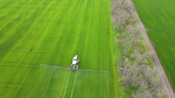 Zicht vanuit de lucht op het sproeien van landbouwtrekkers op het veld, herbiciden en pesticiden bij zonsondergang in de buurt van boomgordel — Stockvideo