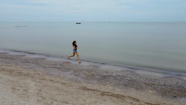 Femme mince courant au ralenti le long des vagues d'eau de mer sur la plage de sable fin. Jolies promenades féminines au surf en bord de mer. Fille après la baignade au bord de l'océan — Video