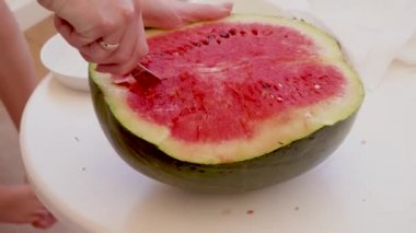 Kadın sulu, tatlı, kırmızı, siyah çekirdekli karpuz hamuruyla kesiyor.