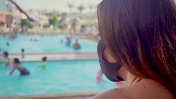 Retrato de mujer de raza mixta con cabello oscuro en el balneario durante el día, con mascarilla facial en contra para prevenir el coronavirus mirando a las personas relajantes en la piscina — Vídeo de stock