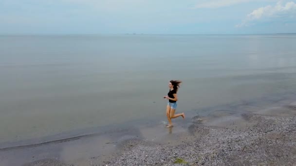 Slim female running in slow motion along sea water waves on sandy beach. Pretty woman walks at seaside surf. Girl after bathing in ocean shore — Stock video