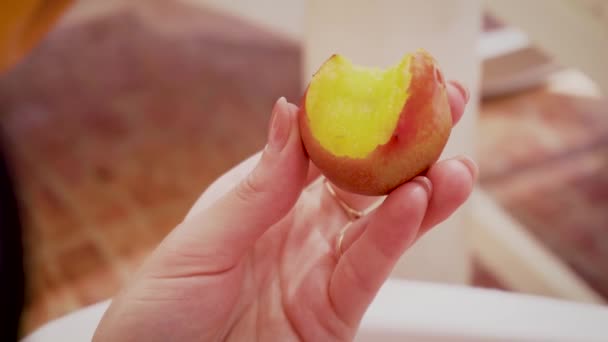 Крупним планом жінка тримає стиглий соковитий персик в руках з кусаною целюлозою, що сидить на довгому ланцюжку — стокове відео