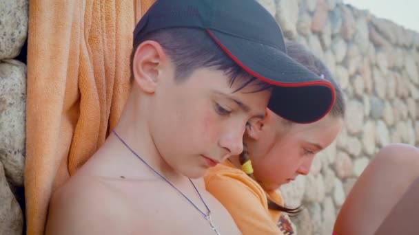 Portraits of lonely children boy and girl sitting next to stonewall. Sad kids brother and sister alone in unknown place — Stock video