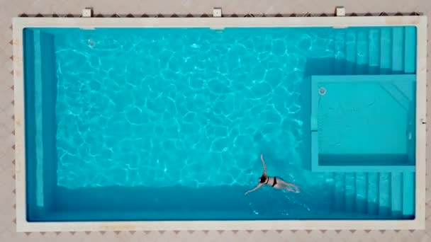 Активна молода жінка плаває в басейні і розбризкує воду. Пані відпочиває на тропічному курорті. Жінка в купальнику в басейні з прохолодною прохолодною водою на сонячний день зверху вниз — стокове відео