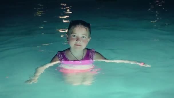 Χαριτωμένο χαμογελαστό κοριτσάκι σε μπλε νερά στην πισίνα τη νύχτα — Αρχείο Βίντεο
