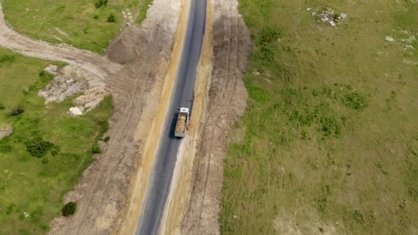 Sand wird für den Bau einer neuen asphaltierten Straße aus dem Korpus eines mächtigen Bergbau-Kippwagens geschüttet — Stockvideo