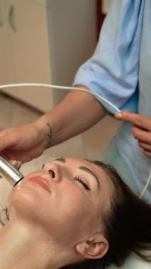 Çene hattında Pressotherapy lenfatik drenajı uygulayan güzellik terapisti, dikey yönelim. Cilt bakımı uzmanı şişkinliği ve toksinleri azaltmak için hava basıncı masajı yapıyor. Soğuk Plazma Derisi ile yüz hatlarını geliştiren estetik uzmanı