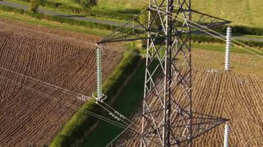 Kapalı elektrik direği ekili tarım arazisinde duruyor. Havadan yüksek voltajlı güç kulesi görünüyor. Ayrıntılı çelik kafes yapısı. Üstten aktarım hatlarını tarlaya taşıyor.
