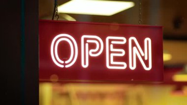 Tahtada açık tabela var. İçerde parlak bir şekilde aydınlatılmış vitrinde asılı. Panelde, neon kelimesinin davetkar akşam ziyaretçileri için açık olduğu görülüyor. Meşgul ticari caddenin penceresinden geçenleri karşılamak için imza atın.