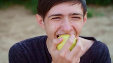 Genç bir delikanlı yeşil elma yiyor, neşeli bir ifadeyle kıtır kıtır ve keskin tadını çıkarıyor. Erkek ısıran yeşil elma, ferahlatıcı ve sulu bir tat. Yeşil elmadan hoşlanan adam, doğal ve canlandırıcı duygulara dalmış.