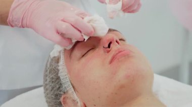 Cilt bakımı sırasında yumuşak bez kullanarak kozmetolog tarafından çıkarılan kremsi yüz maskesi. Müşteri sakin bir şekilde dinlenirken profesyonelce yüz temizleme. Görünüşü iyileştirmek ve cildini tazelemek için tasarlanan tedavi