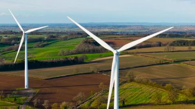 Renkli kırsal bölgelerde dönen yel değirmenleri yenilenebilir elektrik üretiyor. Rüzgar türbinleri parlak gökyüzünün altında dönüyor ve ekolojik enerji üretiyor. Türbin bıçakları yeşil araziyi çeviriyor alternatif çevresel güç sağlıyor