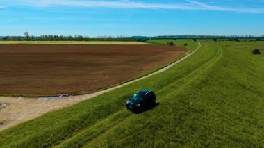 Çiftlik arazileri arasındaki çimenli su setinde SUV sürüyordum. Aracı tarlanın yakınındaki yüksek kırsal yoldan hareket ettiriyor. Tarımsal bölgeleri ayıran kırsal bölgede gezinen bir araç. Yeşil set arazisinde off-road rotasında ilerliyoruz.
