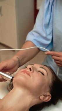 Çene hattında Galvanik Cilt Terapisi uygulayan estetik uzmanı, dikey yönelim. Cilt bakımı uzmanı ürün emilimini arttırmak için düşük seviyeli elektrik akımı kullanıyor. Fraksiyonel RF ile hücresel yenilenmeyi teşvik eden güzellik uzmanı