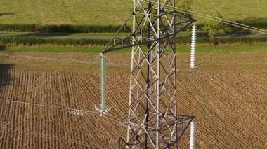 Tarlaların üzerinde duran devasa elektrik direği. Elektrik direği yüksek voltajlı elektrik hattı altyapısını destekliyor. Güçlü çelik iskelet kulesi, ekili alanda asılı kondüktörleri taşıyor.