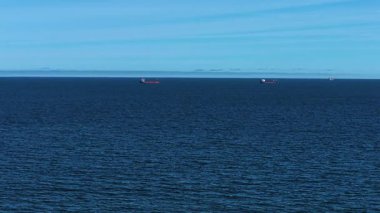 Sakin okyanus yüzeyinde yüzen birkaç kargo gemisi olan deniz burnu. Deniz manzarası derin mavi denize dağılmış büyük uçak gemilerini gösteriyor. Parlak gökyüzünün altında hareket eden yük gemileriyle okyanus ufku. Barışçıl havada açık sularda yüzen ticari gemiler.
