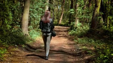 Sessiz toprak yolda, güneşli ormanda yürüyen bir kadın. Ağaçlarla çevrili gölgeli orman patikalarında gezinen dişi. Yeryüzü yolunda huzur içinde yürüyen, yemyeşil çizgili bir kadın.