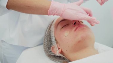 Kozmetik uzmanı yüz yüze krem sürerken cilt bakımı sırasında sakince uzanan kadın. Profesyonel bakım gören kadın, besleyici ve nemlendirici cilde odaklanmış. Cildini geliştirme amaçlı rahatlatıcı güzellik tedavisinden hoşlanan kız