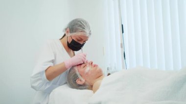 Güzellik uzmanı ergenlik sivilcelerini hassasiyetle ve özenle temizliyor ve cilt dokusunu geliştiriyor. Kadın, derin gözenek tedavisi için temizleme prosedürü uyguluyor. Titiz cilt bakımı sırasında dinlenen kız görüntüyü gençleştirir