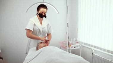 Güzellik uzmanı terapi sırasında genç bir bayanın yüzünü nazikçe tedavi ediyor. Klinik ortamdaki yüz terapisi tekniklerine odaklanan bir uzman. Profesyonel uzmanlığı olan genç yüz üzerinde gelişmiş cilt terapisi uygulayan bir bayan.