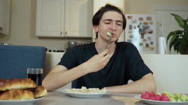 Çatalla salatalık yiyen bir adam. Yemek masasında taze yeşil sebze tadıyor. Yemekte kıtır kıtır salatalık yiyen kişi