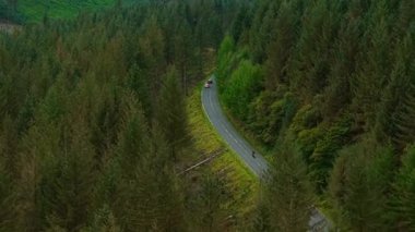 Motosikletli, sık yeşil ağaçlar arasında, dolambaçlı orman yolunda hızlı gidiyor. Sürücü dağ vadisinde özgürlüğünü ifade ederek hızla ilerliyor ve seyahat rahatlığı talebi artıyor. Manzaralı arazide devam eden yolculuk modern dünyayı gözler önüne seriyor.