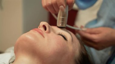 Cilt bakımı kliniğindeki eğitimli güzellik uzmanından rahatlatıcı yüz masajı gören bir kadın. Ultrasonik Cilt Sıkışması, Darsonval Deri Uyarımı. Yüz terapisi, cilt canlandırma, yetişkin müşteriler için gençleri koruyan kozmetoloji, cilt bakımı uzmanı yöntemi
