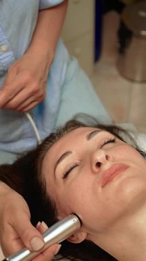 Güzellik terapisti yanakta termal kaldırma terapisi uyguluyor, dikey yönelim. Cilt bakımı uzmanı cildini sıkılaştırmak ve sıkılaştırmak için ısı tabanlı teknoloji kullanıyor. Estetik uzmanı seans sırasında Foton Gençleştirme Terapisi ile yüz hatlarını geliştiriyor.