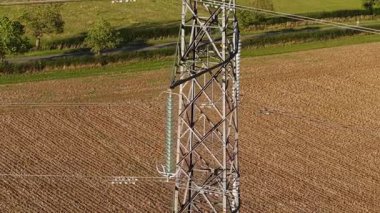 Görünür kablolarla tarım arazisinde duran uzun elektrik direği. Elektrik akımı çelik kafes sütunlarında akıyor. Ağır metal kule, ekili toprağın üzerinde asma güç iletkenleri taşıyor.