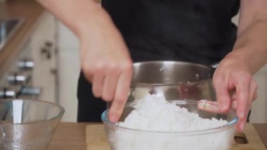 Cam kasede taze pişmiş pilav. Tanımlanamayan kişi buğulanmış tahılları elle kontrol ediyor. Şeffaf konteynırda sıcak pirinçle uğraşıyorum. Pirinç dokusunu suşi yapmak için hazırlıyorum.