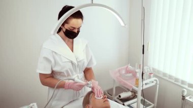 Güzellik uzmanı odaklanmış ifadeyle müşteriye kozmetoloji prosedürü uyguluyor. Sakin bir ortamda profesyonel aletlerle cilt bakımı yapan bir kadın. Gelişmiş kozmetoloji tekniklerini titizlikle ve özenle uygulayan bir bayan.