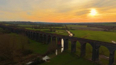 Alacakaranlıkta vadiden geçen demiryolu köprüsü. Çevresinde doğa olan eski tren köprüsü manzaralı drone manzarası. İkonik simgeler, ünlü bölge, yemyeşil manzaralar arasında ulaşım altyapısı