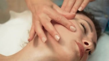 Yüz masajı ve baş masajı için spa yatağında uzanan rahatlatıcı kadın. Masaj terapisti tarafından yapılan yüz bakımı tedavisi. Sağlık vücut masajı ve yüz spa konsepti. Spada masaj prosedürü