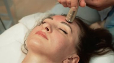Güzellik stüdyosunda uzman bir bayan müşteri yüz terapisinden zevk alıyor. Ultrasound yağ azaltma, yüksek frekanslı yüz terapisi. Yüz bakımı, cilt bakımı, yaşlı kadın için yaş değiştirme tedavisi, güzellik prosedürü.