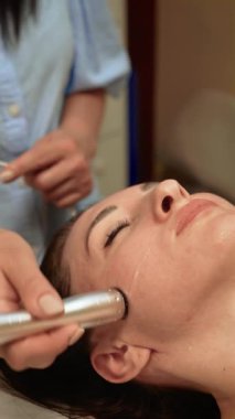 Yanaklara hidroterapi uygulayan estetik uzmanı, dikey yönelim. Cilt bakımı uzmanı su bazlı deriyi temizleme ve hidrat alma yöntemini kullanıyor. Plasma Lift Cilt Yenileme ile Güzellik Uzmanı Cilt Yenileme