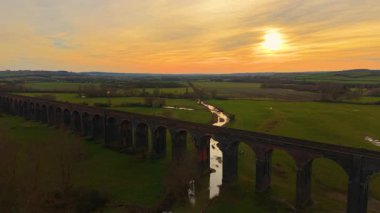 Tarihi demiryolu viyadük, altın gün batımının altında huzurlu vadiyi geçiyor. Demiryolu turuncu gökyüzünün altında manzaralı viyadük geçidi. Sonsuz tuğla köprü sıcak alacakaranlıkta kırsal kesimlere doğru uzanıyor.