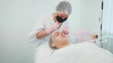 Kadın kozmetikçi, hastanın sorunlu derisinden iltihap dolu sivilceleri alıyor. Kadın dermatolog hastasının sorunlu cildinde iltihaplı sivilceleri tedavi ediyor. Bayan kozmetikçi, ziyaretçinin sorunlu cildinin lekelerini temizliyor.