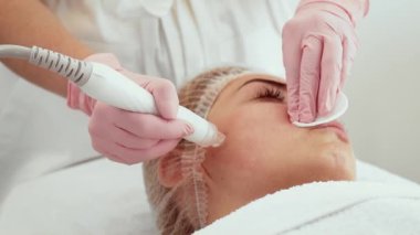 Güzellik uzmanı kadın dermatoloji ofisinde sıvı temizleme cihazı uyguluyor. Deri yenileme seansı sırasında hasta rahat bir şekilde yalan söylüyor. Tedavi gözeneklerin temizlenmesine ve cilt görünümünün iyileştirilmesine yardımcı olur