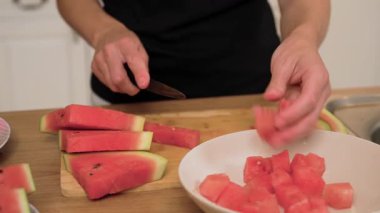 Karpuz küplerini beyaz kaseye koymak. Yeni kesilmiş bir parçayı elimde tutuyorum. Sulu kırmızı meyve dilimledikten sonra düzenlenir. Masada servis için tatlı parçalar hazırlıyorum.