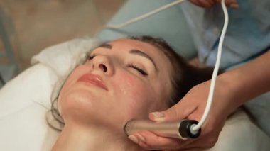 Lisanslı cilt bakımı uzmanından sakinleştirici yüz masajı alan bir bayan. Elektrostimülasyon Cilt Gençleştirme, Ultrasonik Cavitation RF Terapisi. Yüz güzelleştirme, cilt yenileme, yetişkin kadınlar için gençlik artırıcı estetik, kozmetik