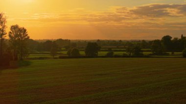 Tarım arazisinin üzerinde buğday tarlasıyla gün batımı. Kırsal alanda altın akşam ışığı ve hasat edilmiş mısır gevreği. Kesilmiş buğday sakalıyla tarlaların üzerinde sıcak ufuk parıldıyor