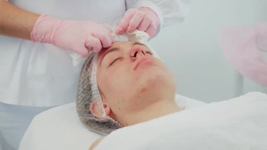 Modern klinikte yumuşak mendil kullanarak kozmetik uzmanı tarafından yapılan cilt temizleme. Müvekkil rahat yatarken profesyonelce arınmaya odaklanmak. Rahatlama oturumunda cilt sağlığını ve tazeliğini iyileştirmeyi amaçlayan tedavi