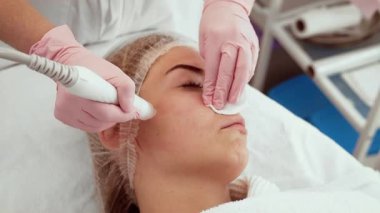 Güzellik uzmanı kadın kozmetoloji stüdyosunda Hydra yüz aygıtı kullanıyor. Hasta nazik cilt bakımı görüyor. İşlem cildin temizlenmesine ve su içilmesine yardımcı olur.