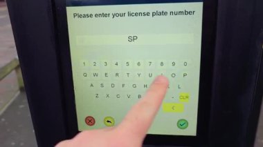 Tanımlanamayan kişi, plaka numarasını parkmetre ekranından giriyor. Dokunmatik ekran tuş takımı park alanındaki park ücretini işliyor. Otomatik park terminali kullanan isimsiz sürücü park aracı