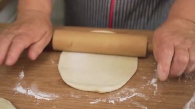 Küçük hamuru raptiyeyle yuvarlıyor. Masada tanınmayan birinin hamur düzleştirmesi. Yuvarlak parçayı ince bir çarşafa bastırıyorum. Ev yapımı börekler için hamur hazırlıyorum.