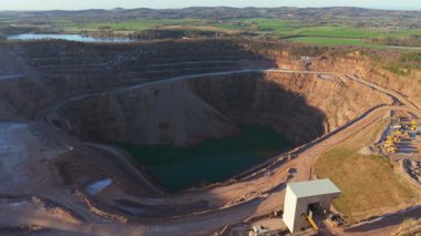Derin kazılar etrafında çalışan ağır makineli açık maden ocağı. Teraslı kaya yollarında çalışan endüstriyel ekipmanlı büyük ölçekli taş ocağı madenciliği. Taş ocağının içinde hareket eden kamyonlarla birlikte açık çukur madenciliğinin hava görüntüsü.