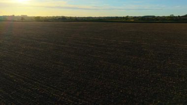 Temiz ekilebilir arazi, akşam ışığında yeni ekilmiş tarla. Sıcak günbatımı gökyüzünün altında açık tarım arazisi boyunca yumuşak toprak yüzeyi. Gece geç saatlerde tarıma hazırlanan kara desenli toprak