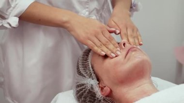 Güzellik salonunda cilt gençleştirme ve esneklik geliştirme prosedürü uygulanıyor. Profesyonel terapist, kolajen üretimini teşvik etmek ve yüz hatlarını sıkılaştırmak için nazik masaj teknikleri uyguluyor. Rahatlatıcı atmosfer ve kişisel yaklaşım