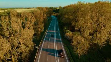 Çekici karavanı ormanlık alanda boş bir yol boyunca sürüyor. Taşıt akşam ışığında kırsal yolda hareket ediyor. Ağaçlar ve tarım arazileri arasında kargo taşıyan yolcu vagonu.